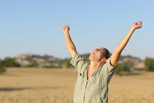 Excited woman raising arms in a field on summer