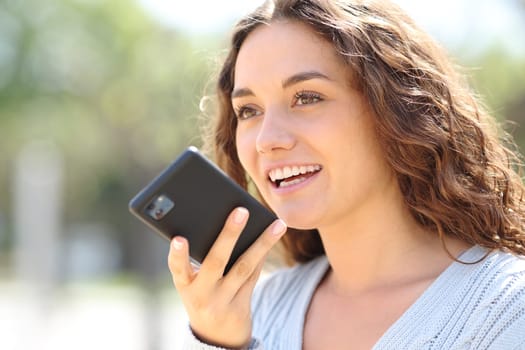 Woman smiling while is dictating message on phone in the street