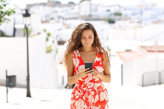 Front view portrait of a tourist walking and using smart phone in a white town on vacation
