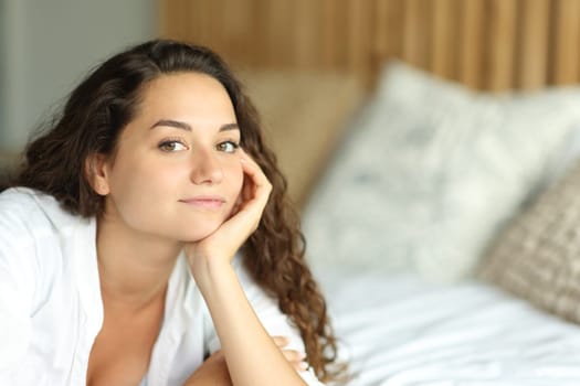 Relaxed woman looking at camera lying on the bed in a bedroom