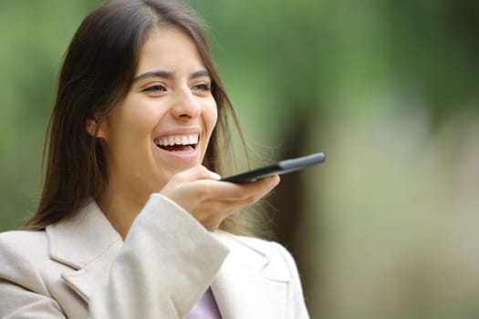 Happy woman using voice recognition with smart phone in winter