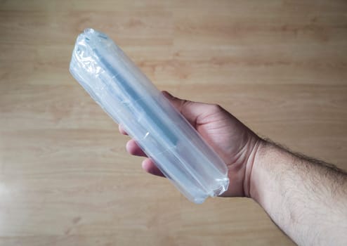 Hand holds a product wrapped with inflatable packaging columns bags. Wooden floor background