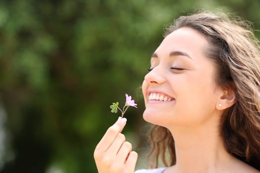 Happy candid woman smelling little flower in a park