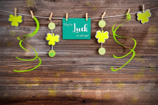 Saint Patrick's Day Green Label With English Text May The Luck Be With You Vintage Wooden Background With Decorative Clover And Shamrock.