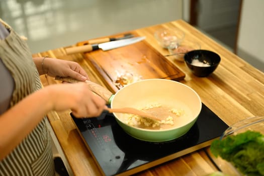 Close up of adult woman stirring ingredients in a frying pan while preparing delicious meal.