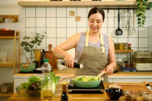Smiling adult woman adding soy sauce into a pan with vegetables while cooking a healthy meal.