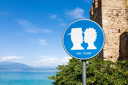 Kiss street sign located in public area in front of Sirmione castle, Italy. Concept of love, couple, romantic