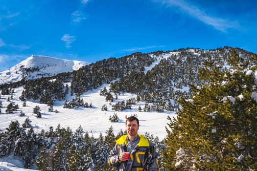 Men drinking coffee or tee, smiling and looking at camera, snowy forest and mountains in background. Winter ski holidays, Andorra, El Tarter, Pyrenees