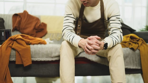 Young man sitting on the edge of a messy couch and looking exhausted.