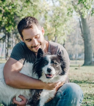 Man with his dog playing outdoor in the park. Young owner hugs his pet in nature.