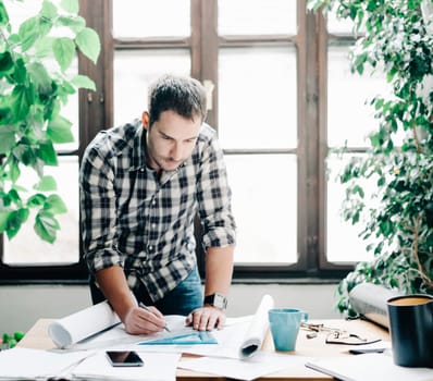 Young man architect working on architectural project in design studio. Modern office concept with green plants.