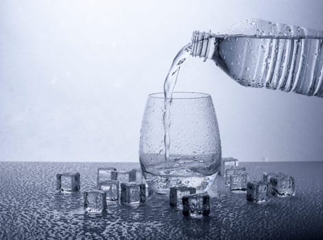 Pouring fresh drinking mineral water from plastic bottle. Glass filled with water over white background.