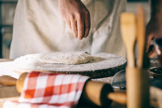 Man kneading and baking homemade pizza dough in the kitchen. Closeup on baker's hands preparing loaf of bread. Cooking and food preparation at home.