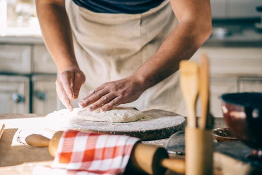 Man kneading and baking homemade pizza dough in the kitchen. Closeup on baker's hands preparing loaf of bread. Cooking and food preparation at home.