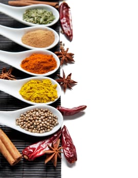 Top view on mixed dry colorful spices in spoons isolated on white background. Indian food and oriental cooking ingredients. Asian restaurant food menu design. Curry, chili, paprika, pepper, cinnamon.