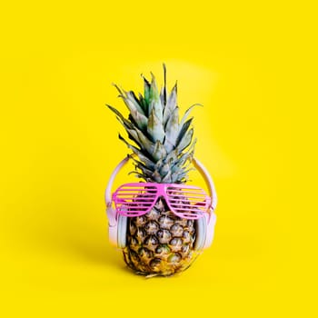 Fashionable  trendy pineapple fruit with headphones and sun glasses listen to the music over bright pastel yellow background. Cool hipster ananas with funny face. Summer holiday vacation and tropical beach party concept.