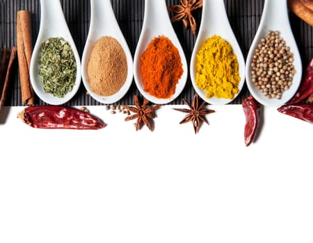 Top view on mixed dry colorful spices in spoons isolated on white background. Indian food and oriental cooking ingredients. Asian restaurant food menu design. Curry, chili, paprika, pepper, cinnamon.