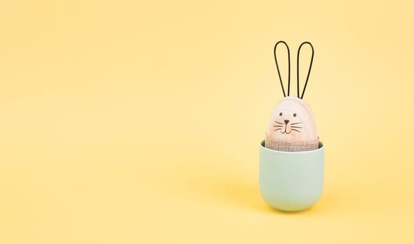 Cute easter bunny or rabbit with a smiling egg face in a cup, spring holiday, greeting card