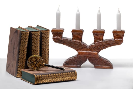 Ancient books with a magnifying glass and a antique wooden candle holder on a bright table isolated on a white background.