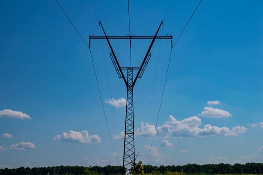 Tower with high-voltage energy transmission wires against the blue sky. High-voltage tower. Electrical wires and fuses. Energy business. Energy industry. Import and export of energy. Blue sky.