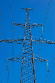 Tower with high-voltage energy transmission wires against the blue sky. High-voltage tower. Electrical wires and fuses. Energy business. Energy industry. Import and export of energy. Blue sky.