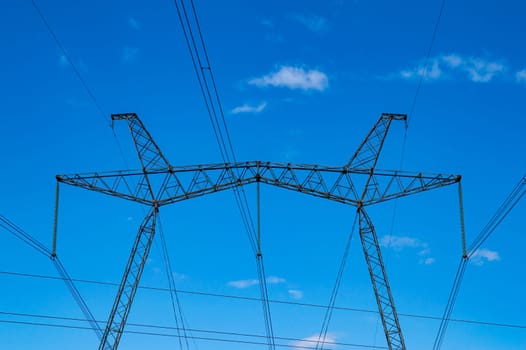 Tower with high-voltage energy transmission wires against the blue sky. High-voltage tower. Electrical wires and fuses. Energy business. Energy industry. Import and export of energy. Blue sky.