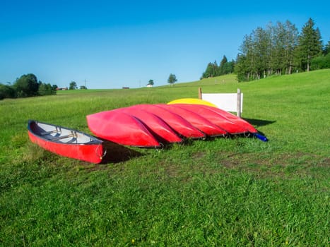 View of a row of red kayaks on a sloping meadow at Grüntensee in Bavaria in summer.
