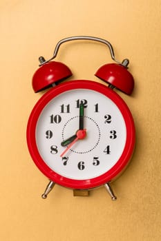 Red alarm clock lying on the golden metal background