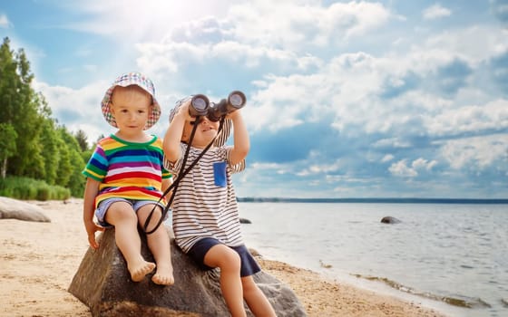 Two children sitting on the stone on the seacoast in summer. Concept of the family vacation and tourism.