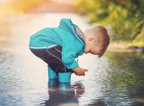 Cute little child standing in the puddle and playing with rainwater. Toddler walking in nature after rain.