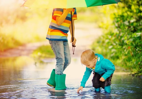 Two brothers standing with rainbow umbrella in the puddle. Concept of the family relation and love.