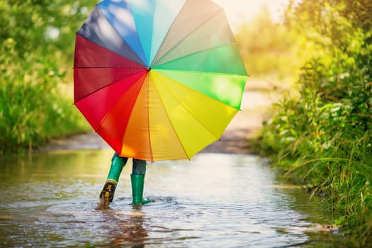 Boy walking through the puddle with colorful umbrella in his hands. Concept of the happiness childhood.