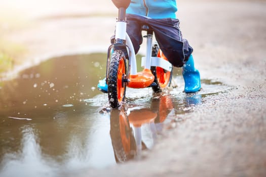 Child on the balance bike riding through the puddle. Concept of the childhood and recreation.