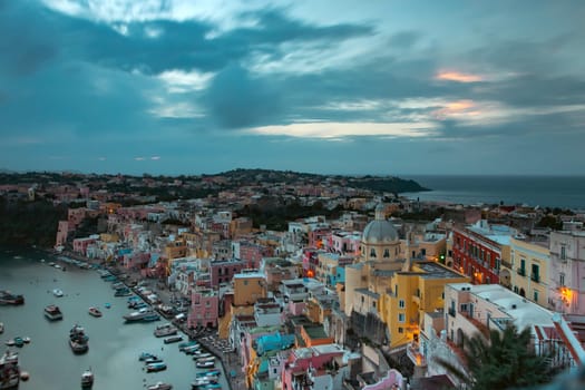 View of the Port of Corricella with lots of colorful houses after sunset in Procida Island, Italy.