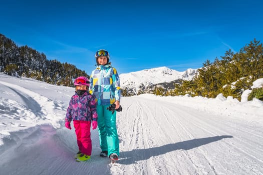 Mother and daughter, family, standing on a snowy road with forest and mountains in background. Winter ski holidays, El Tarter, Andorra, Pyrenees