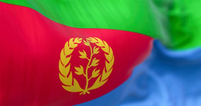 Close-up view of the Eritrea national flag waving. Eritrea flag is red triangle on hoist, green & blue triangles, gold emblem of olive branch & wreath. Fabric textured background. Selective focus