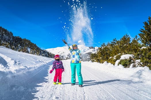 Mother and daughter, family, throwing snow powder up to the air, forest and mountains in background. Winter ski holidays, El Tarter, Andorra, Pyrenees