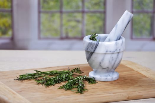 Rosemary herbs and a mortar and pestle on a wooden chopping board in a traditional kitchen