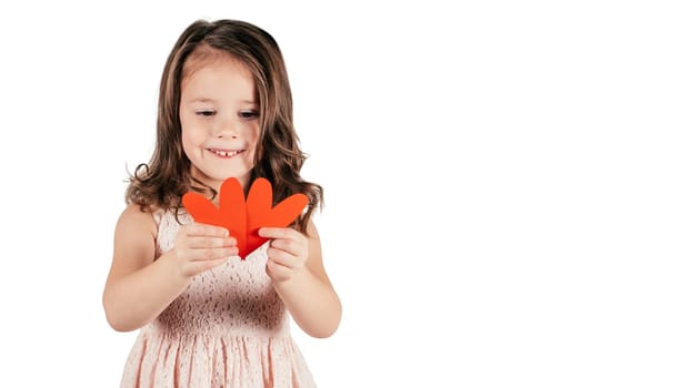 Portrait of little girl with long curly hair hold two red paper hearts together lowering eyes smiling isolated on white background. Family, love, holidays, birthday, Mother's day concept. Copy space