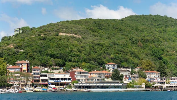 View from the sea of the green mountains of the Europian side of Bosphorus strait, with docked boats, traditional houses and dense trees in a summer day, Istanbul, Turkey