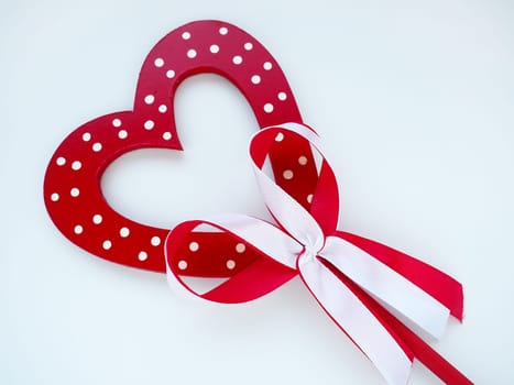 Valentine's day concept. Red wooden heart with white dots and ribbon bow on a stick. White background. A beautiful bow as a decoration. Love and relationships. Recognition or congratulations.