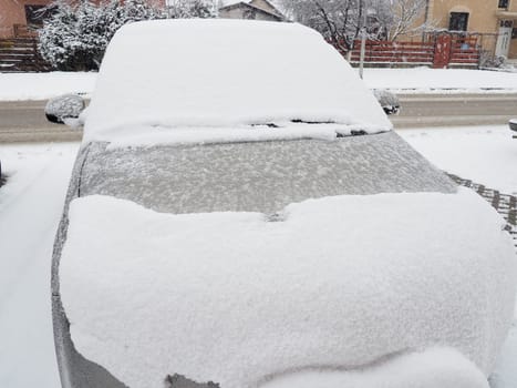 Snow and ice on the windshield, retrovisors and rear-view mirrors of the car. Winter driving conditions. Snow cleaning. Road traffic in winter. Metallic car. Snowdrifts and slush