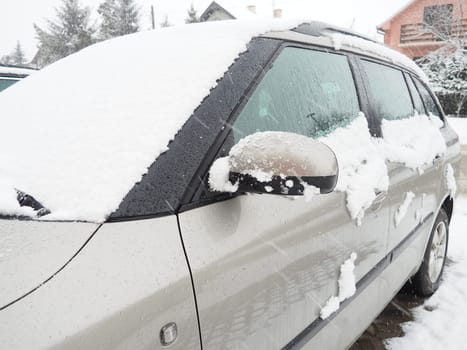 Snow and ice on the windshield, retrovisors and rear-view mirrors of the car. Winter driving conditions. Snow cleaning. Road traffic in winter. Metallic car. Snowdrifts and slush