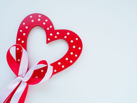 Valentine's day concept. Red wooden heart with white dots and ribbon bow on a stick. White background. A beautiful bow as a decoration. Love and relationships. Recognition or congratulations.