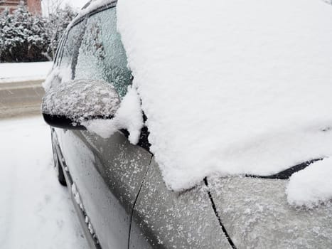 Snow and ice on the windshield, retrovisors and rear-view mirrors of the car. Winter driving conditions. Snow cleaning. Road traffic in winter. Metallic car. Snowdrifts and slush