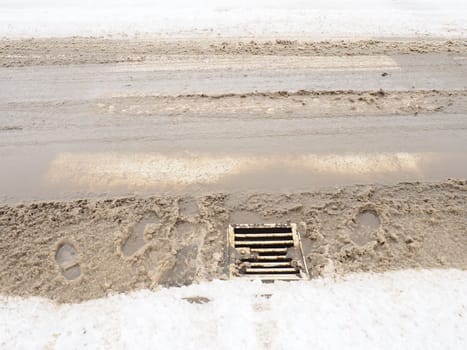 Snow, ice, slush and winter mud at a pedestrian crossing. The air temperature is about 0. Difficult driving conditions. Braking distance of the car. Underground drain with metal grate. Snow melting.