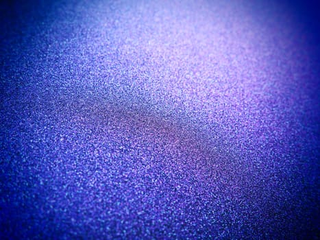 Deep blue. Texture of rough paper or cardboard. Defocused bokeh sparkles and shining. Festive blue background with illuminated sapphire gradient.