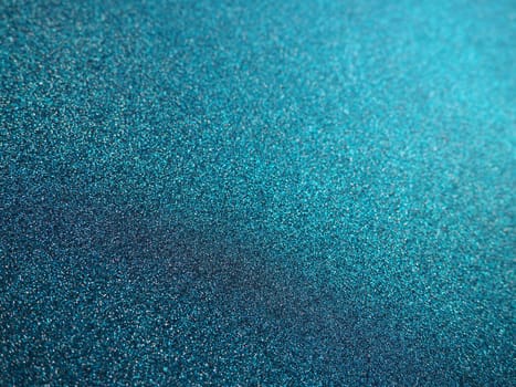 Deep blue. Texture of rough paper or cardboard. Defocused bokeh sparkles and shining. Festive blue background with illuminated sapphire gradient.