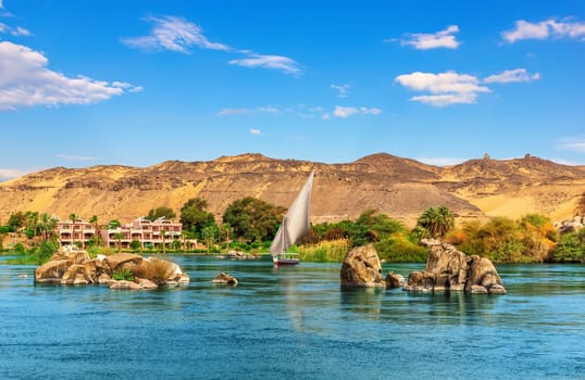 Nile stones and riverbank near Aswan and traditional sailboat, Upper Egypt.