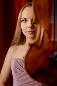 Portrait of young woman musician holding violin front of camera. Music playing and practice concept